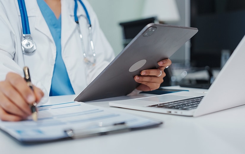 Doctor using tablet and laptop for patient records.